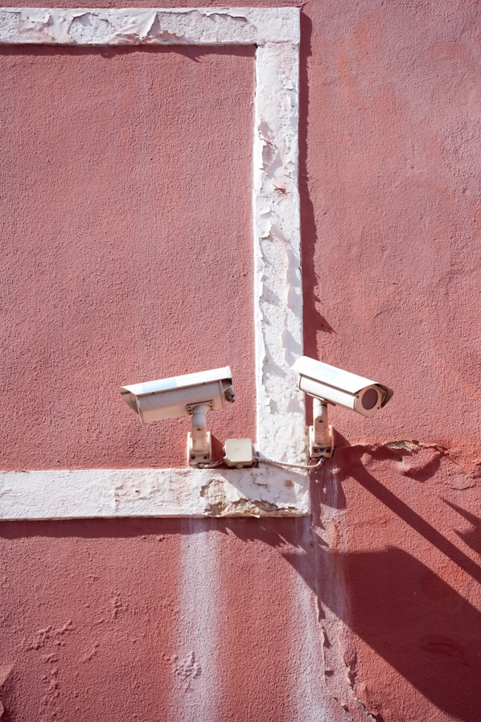 two security cameras mounted to a pink wall
